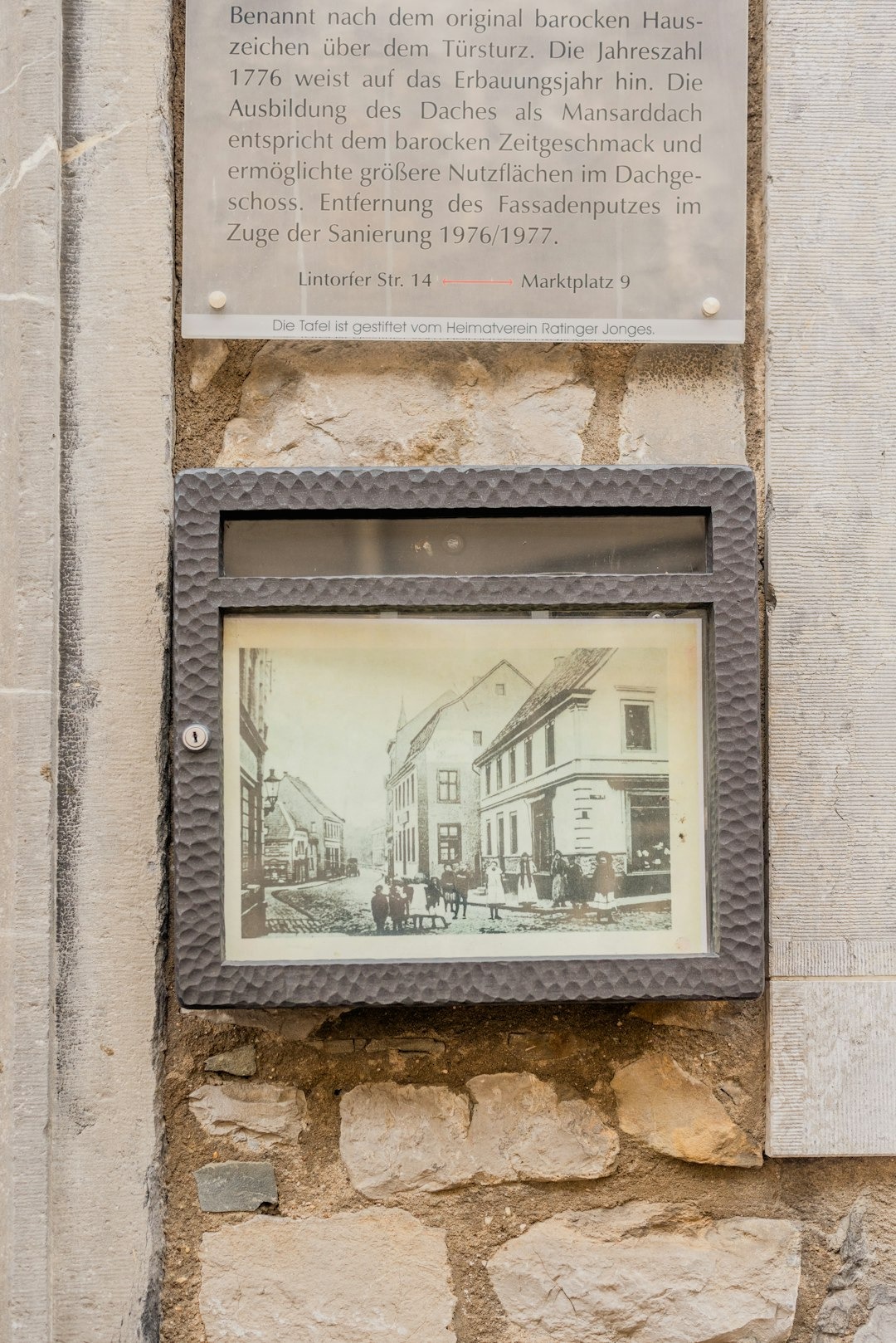 Historical plaque and old photograph mounted on stone wall.